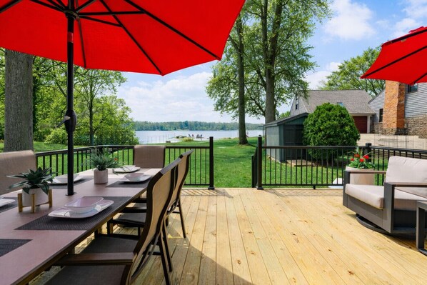 A deck with outdoor furniture, red umbrellas, and a view of a lake.