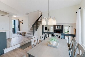 A spacious living area with a dining table, chairs, a staircase, and a fireplace.