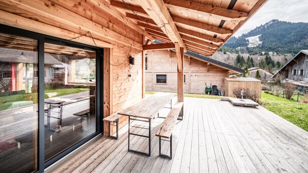 Eine Holzterrasse mit Sitzgelegenheiten im Freien und einer Glastür, die zu einer Patio führt.