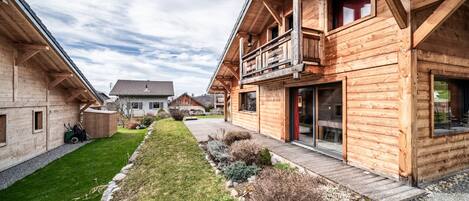 Een houten gebouw in chaletstijl met een balkon, een overdekte veranda en een verzorgd gazon.