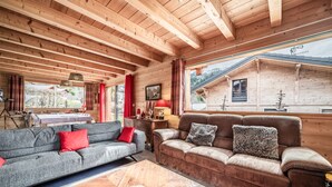 Ein Holzblock-Interieur mit zwei Sofas, einem Couchtisch und einem Fenster mit Blick auf ein Haus.
