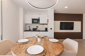 A modern dining area with a wooden table set for four, a kitchen in the background, and a flat-screen TV mounted on the wall. - Apartment in Albufeira with pool (Albufeira)