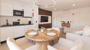 Une cuisine moderne équipée d’un four à micro-ondes, d’une cuisinière et d’un évier. On y trouve un coin repas avec une table ronde en bois et des chaises blanches. Un téléviseur à écran plat est fixé au mur, au-dessus de la table.