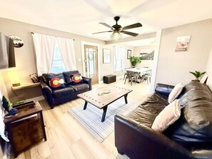 Ein Wohnzimmer mit einer Couch, einem Couchtisch, einem Deckenventilator und einem Essbereich im Hintergrund.