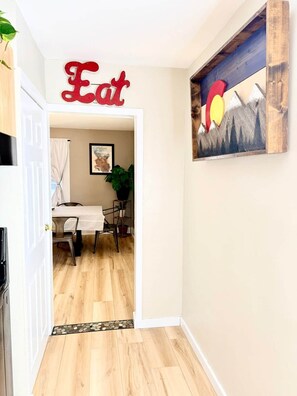 Ein Flur mit Holzboden, ein Essbereich mit Tisch und Stühlen, ein Gemälde an der Wand und ein Schild mit dem Wort 'Eat'.