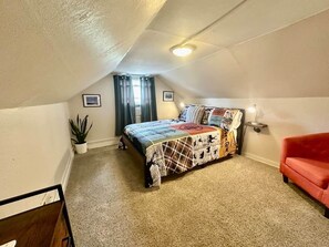 Ein Schlafzimmer mit einem Bett, einem roten Sessel, einer Zimmerpflanze und einer Deckenleuchte.