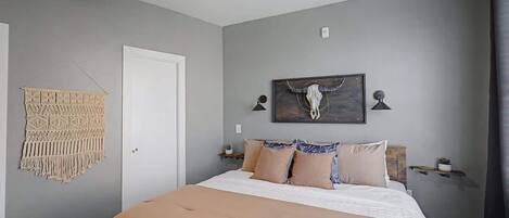 A bedroom with a bed, a ceiling fan, a macrame wall hanging, and a skull artwork on the wall.