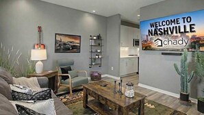 Un salon moderne avec un canapé, des fauteuils, une table basse et un tableau. Un panneau d’accueil indiquant l’entrée de Nashville est accroché au mur.