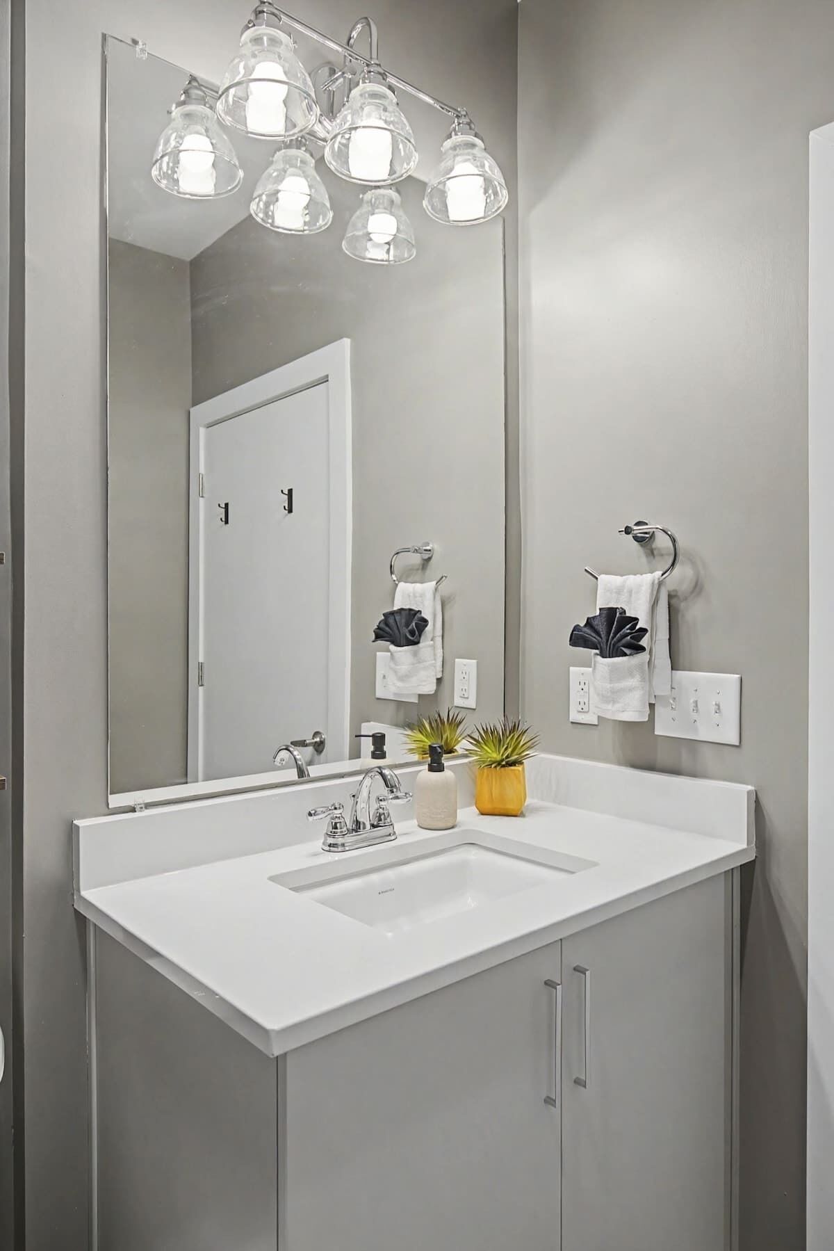 Une salle de bain moderne avec un lavabo blanc, un grand miroir et un luminaire fixé au plafond.