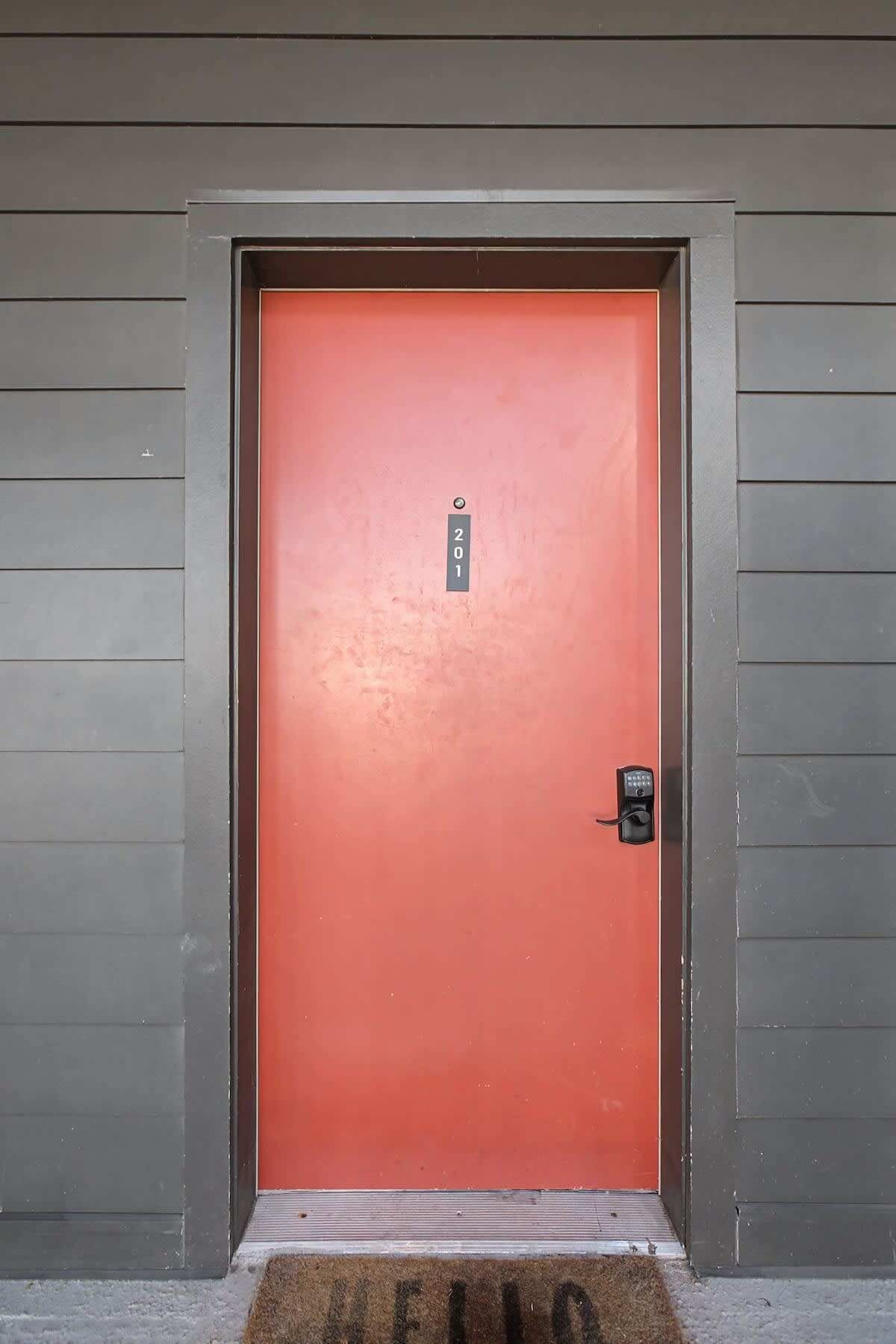A red door with a number plate, a doorbell, and a doormat with the word "WELCOME".