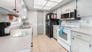 Une cuisine moderne avec des meubles blancs, un réfrigérateur noir, un four à micro-ondes, une cuisinière et une machine à café.