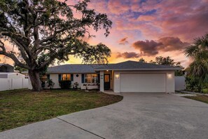 A single-story house with a garage, a driveway, and a large tree in the front yard. - Beach Days & Pool Nights | 3BR Home Near AMI (Bradenton)