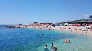 Una spiaggia con acqua cristallina, persone che nuotano e si rilassano al sole, e numerosi ombrelloni.