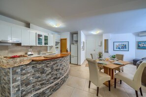 Una cucina moderna con isola in pietra, pensili bianchi e zona pranzo con tavolo e sedie in legno.