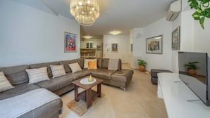 Uma sala de estar moderna com um sofá seccional, uma mesa de centro, uma TV e um candelabro.