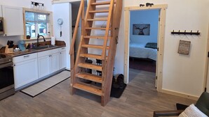 A kitchen with white cabinets, a wooden ladder, a sink, and a window.