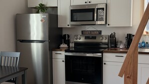 Een keuken met een roestvrijstalen koelkast, een magnetron, een fornuis, en een bord boven het fornuis waarop 'Sockeye Salmon' staat.