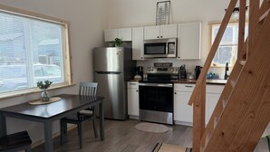 Een compacte keuken met een koelkast, magnetron, oven en een eettafel met stoelen.