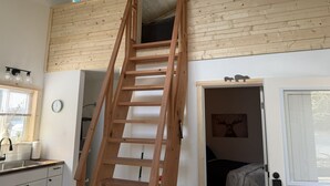 Een kamer met een houten trap naar een vide, een raam met luiken, een wastafel en een klok aan de muur.