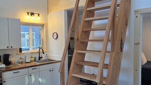 Una cucina con mobili bianchi, un piano di lavoro in legno, un lavello e una scala appoggiata al muro.