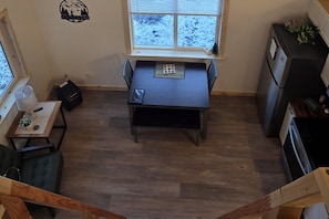 A compact kitchen with a dining table, a refrigerator, and a window with a view of a snowy landscape.