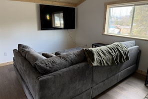 A living room with a sofa, a television mounted on the wall, and a window with a view.