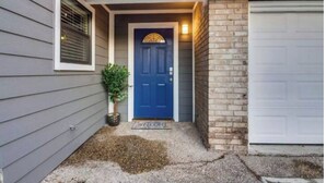 Une maison avec une porte bleue, une petite plante en pot et un paillasson sur lequel est écrit « BIENVENUE ».