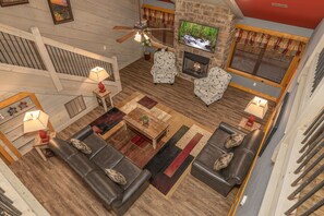 A spacious living room with a fireplace, comfortable seating, and a television mounted on the wall. - Bears Haven – Elegant 3 BR Chalet. Game Area, Hot Tub, see through fire place (Gatlinburg)