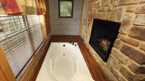 Un baño con pared de piedra, chimenea y ventana con persianas.