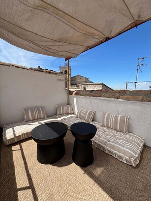 Eine Dachterrasse mit einer Sofagarnitur, zwei runden Tischen und einer großen Markise.