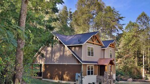 A two-story house with a sloped roof, a garage, and a stone foundation. - Misty Mountainside–Romantic 2-Suite Modern Chalet with Hot Tub and Pool Table (Gatlinburg)