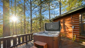 A hot tub on a wooden deck with a view of a forest and a cabin. - Bucky’s Blind · Cozy Forest Escape: Hot Tub, Playground, Fire Pit (Broken Bow)