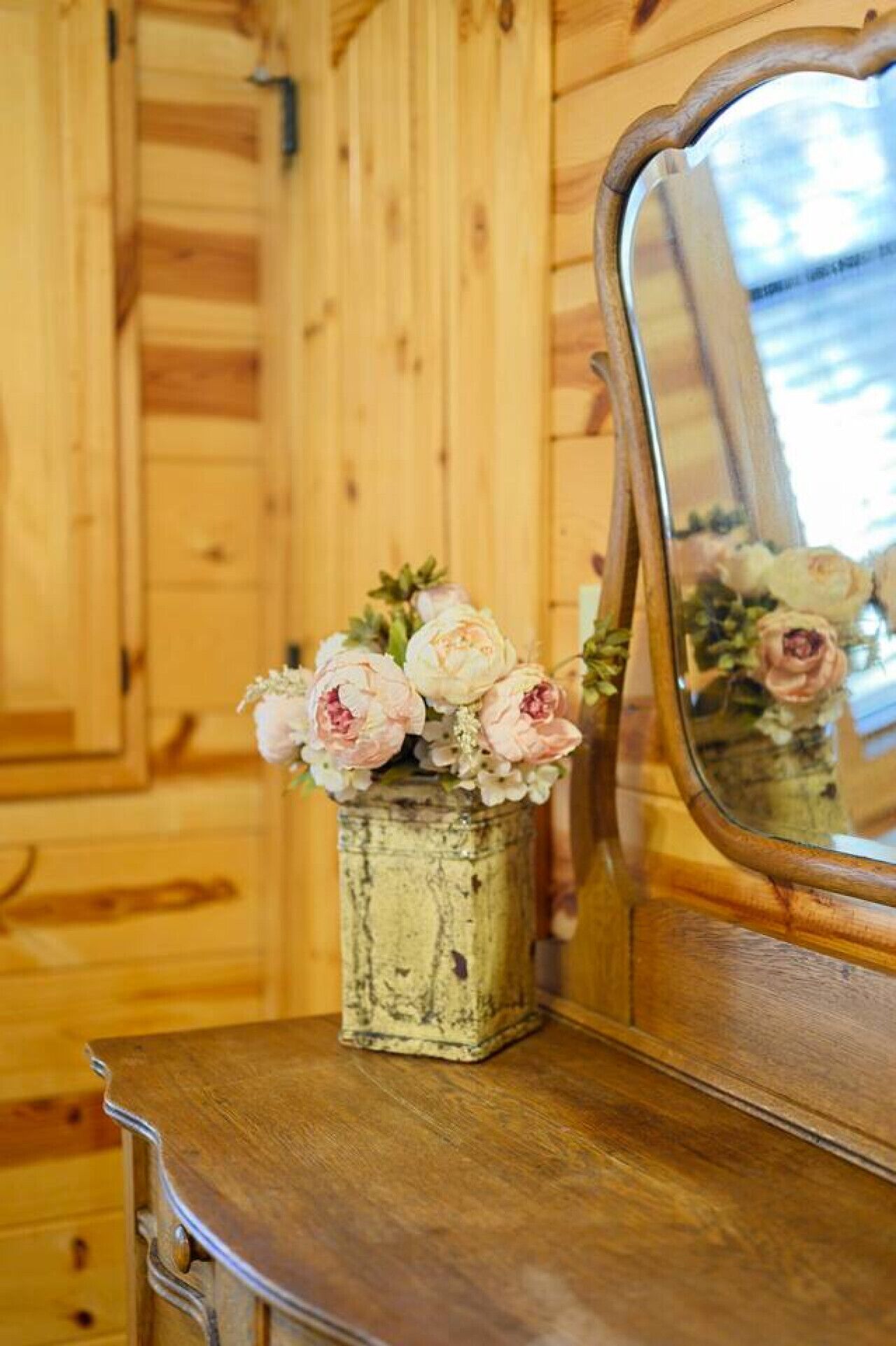 A rustic wooden dresser with a mirror reflecting a vase of flowers.