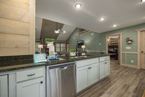 A kitchen with a dishwasher, granite countertop, and a dining area with a table and chairs. - Smoky Pines Chalet – Modern 3-BR  with Hot Tub, Game Room and Resort Pool (Gatlinburg)