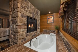 Ein Badezimmer mit Steinwänden, einer großen Badewanne, einem Kamin und Holzvertäfelung.