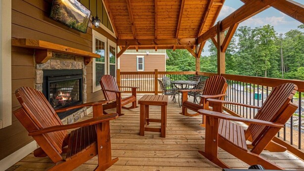 A wooden deck with Adirondack chairs, a stone fireplace, and a table.