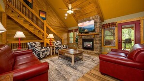 A spacious living room with a stone fireplace, a wooden staircase, and leather sofas.