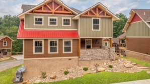 A two-story house with a red roof, stone foundation, and a stone wall in front. - Altitude Adjustment – 4BR Chalet Indoor Pool with Theater Room (Gatlinburg)