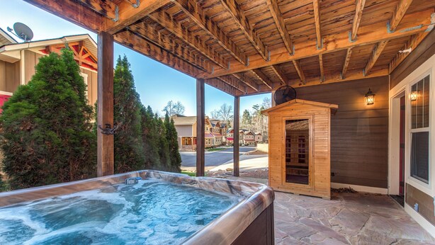 A hot tub under a wooden pergola with stone flooring, surrounded by a residential neighborhood.