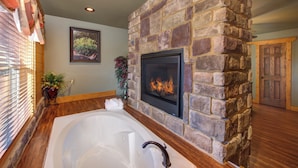 A bathroom with a stone fireplace, a bathtub, and wooden flooring.