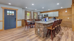 A spacious kitchen with a central island, wooden cabinets, and a blue door.