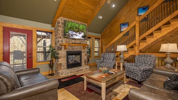A cozy living room with a stone fireplace, wooden ceiling, and a staircase.