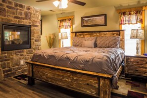 A bedroom with a stone wall, a wooden bed frame, a ceiling fan, and a fireplace. - Gatlinburg Pool Pad | Indoor Pool • Sauna • Theater • Sleeps 10 (Gatlinburg)