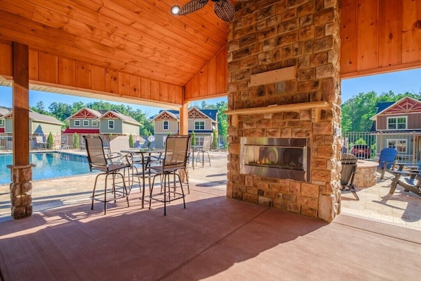 A covered outdoor area with a stone fireplace, pool, and patio furniture.