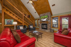 A spacious living room with a fireplace, leather sofas, a coffee table, and a staircase leading to an upper level. - Luna Bear Lodge – Luxury 4BR Chalet w/ Indoor Pool, Game Room & King Suites (Gatlinburg)