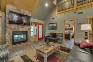 A spacious living room with a stone fireplace, a flat-screen TV, a wooden coffee table, and a leather sofa. - Marco Polo | Luxury 4BR Chalet w/ Indoor Pool, Theater Room & Mountain Views (Gatlinburg)