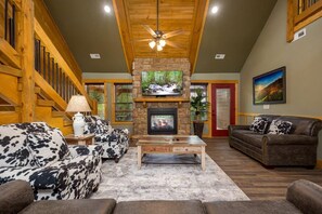 A cozy living room with a stone fireplace, wooden ceiling, and a TV mounted above it. - Mountain Palace - Indoor Pool, Theater, Game Room, Hot Tub, fire place (Gatlinburg)