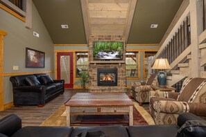 A spacious living room with a stone fireplace, comfortable seating, and a television. - Serenity Peak -Lux Chalet, Indoor Saltwater Pool, Sauna, Theater & Game Loft (Gatlinburg)