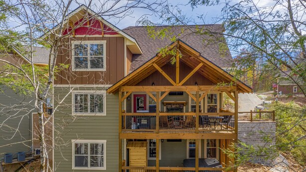 A two-story wooden cabin with a balcony on the upper floor, a front porch, and a small attached garage.