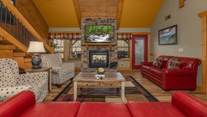 A cozy living room with a stone fireplace, a red leather sofa, patterned armchairs, and a wooden coffee table.